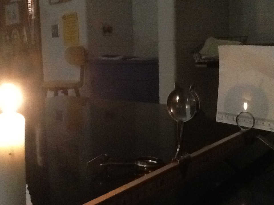A candle burns, and a converging lens makes a real image of it on a screen. Note the image is upside down